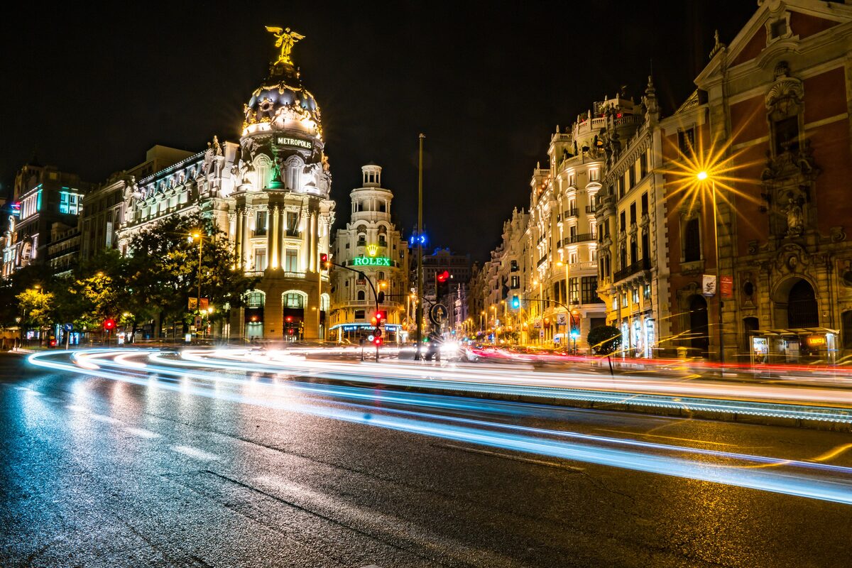 The Metrópolis building lit up at night on the Gran Vía, with traffic light trails in the foreground
