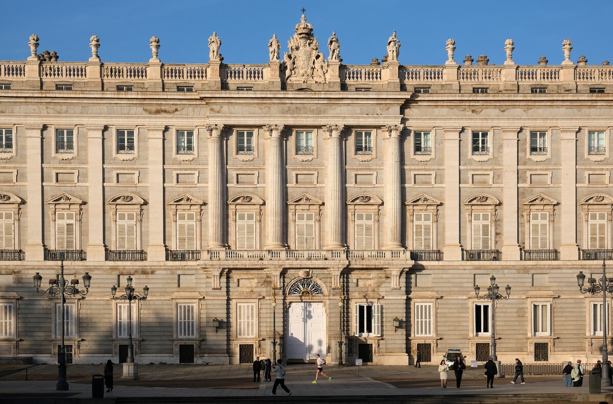 The Royal Palace's east facade in warm afternoon light, with columns, balustrade statues and a few people walking along its foot