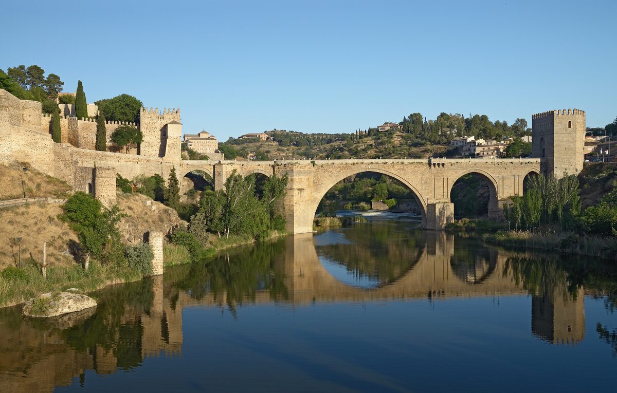 The San Martín bridge and its gate towers in evening light, reflected in the calm Tagus