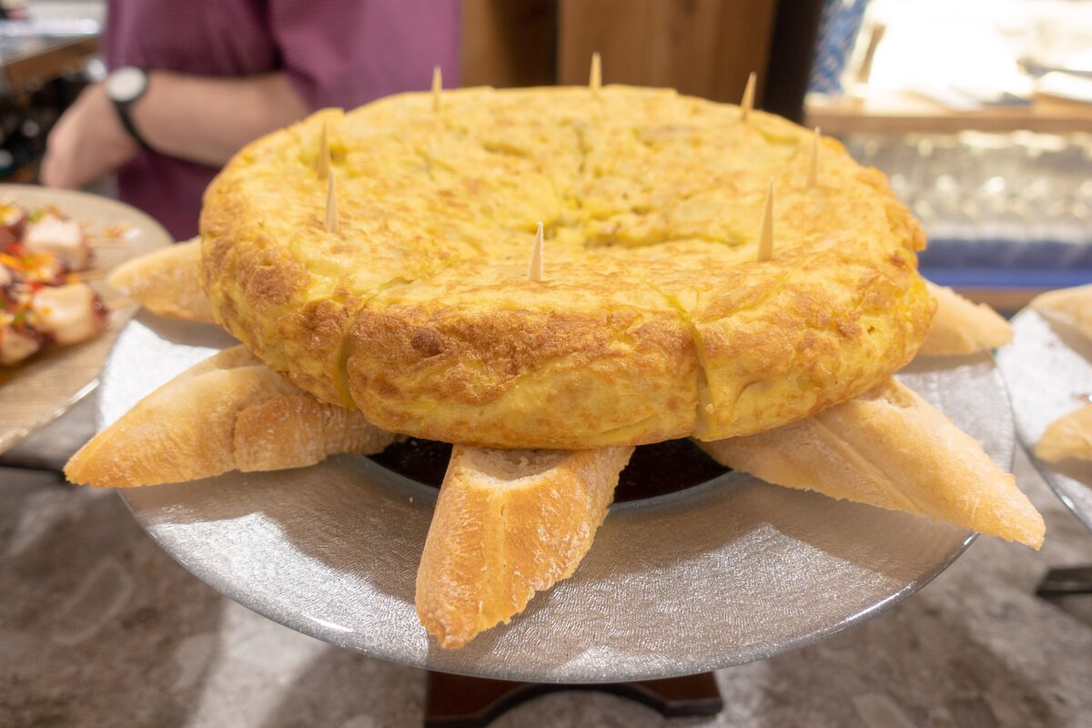 A whole thick Spanish omelet on a plate, ringed by slices of bread