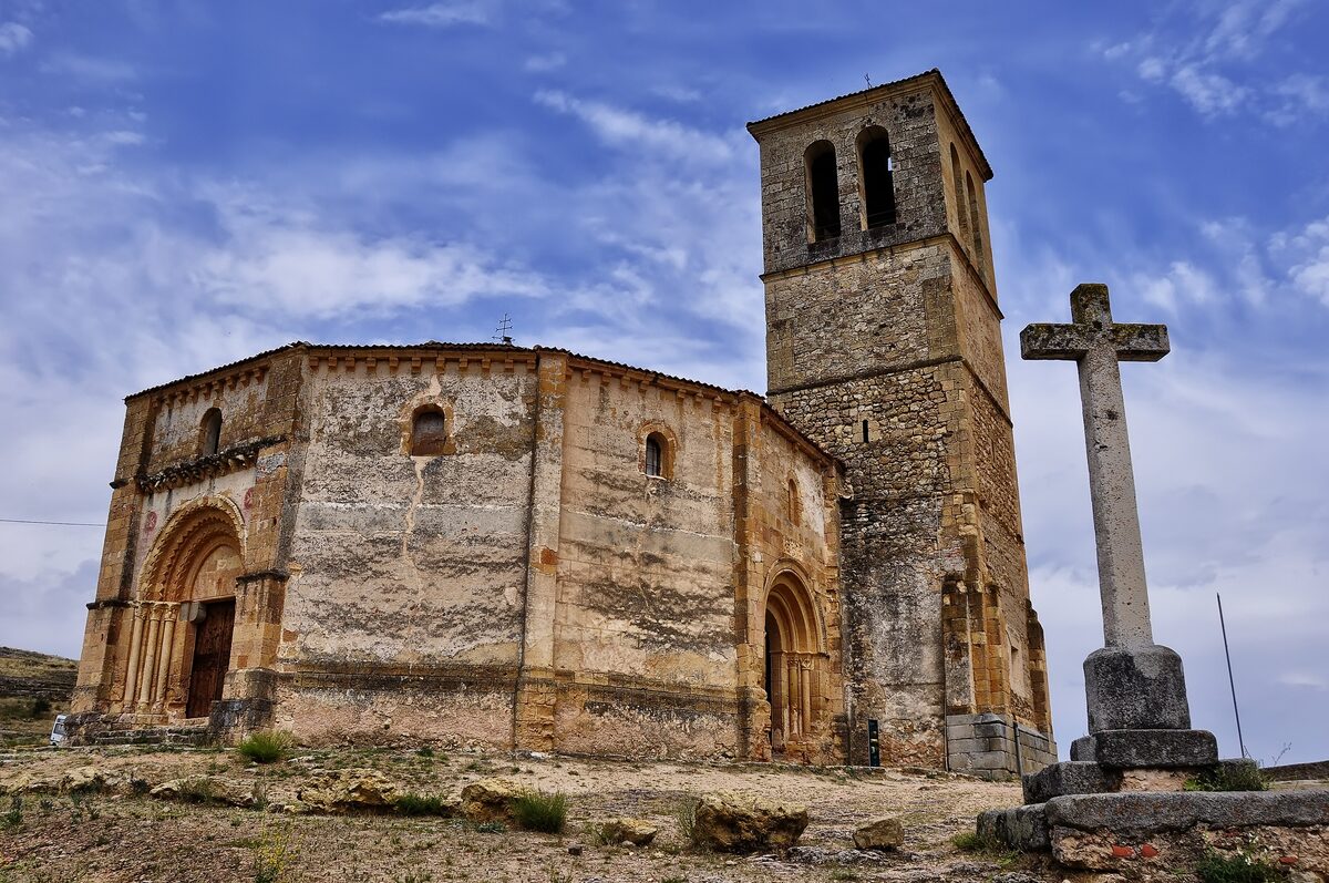 The twelfth-century Vera Cruz church with its squat tower and a stone cross in front, under a blue sky