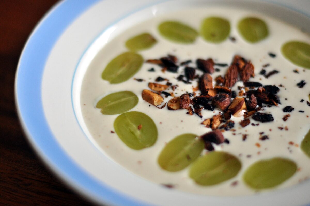 A bowl of white almond soup topped with green grapes and toasted almonds