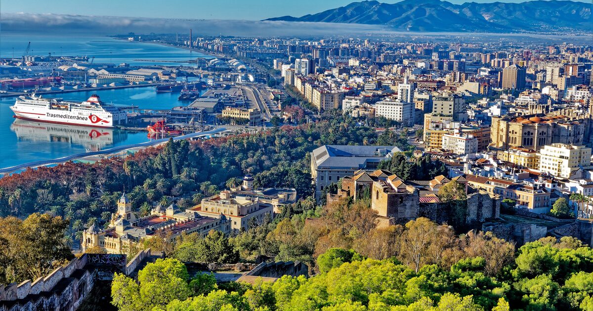 Málaga from the castle walls: the Alcazaba among pines, cathedral roofs, a ferry in the port and mountains behind