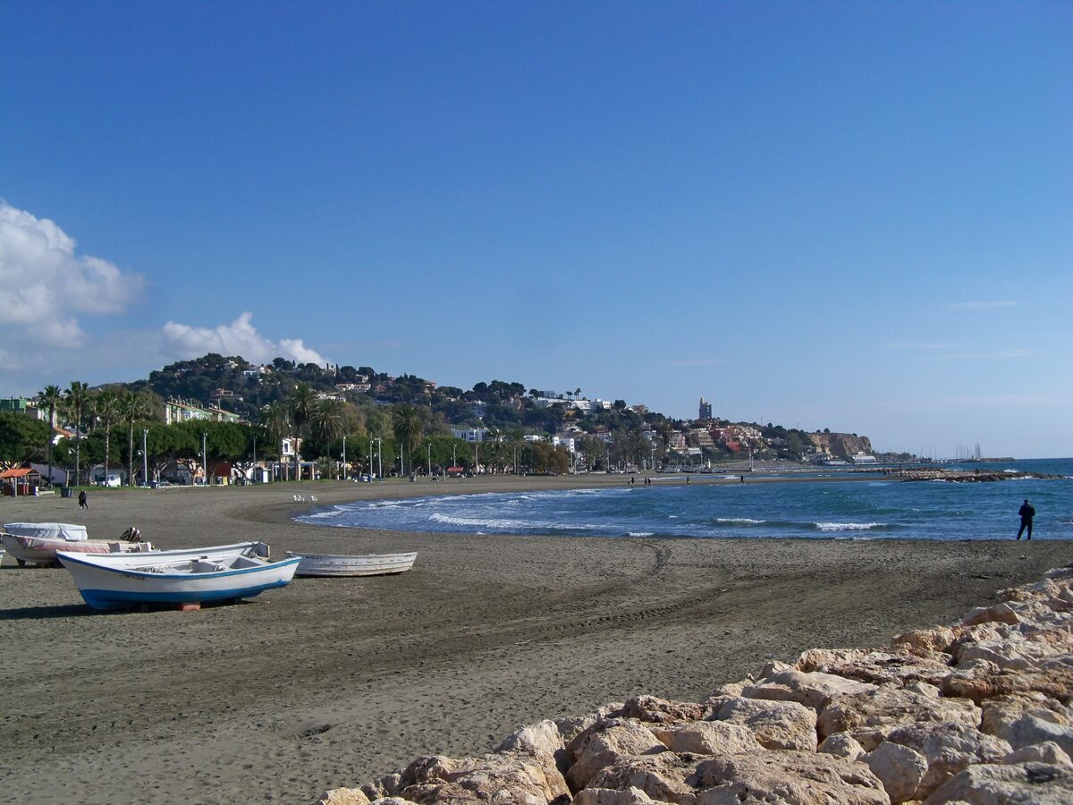 Fishing boats pulled up on the sand at El Palo beach, with the sea and the town on the hill behind