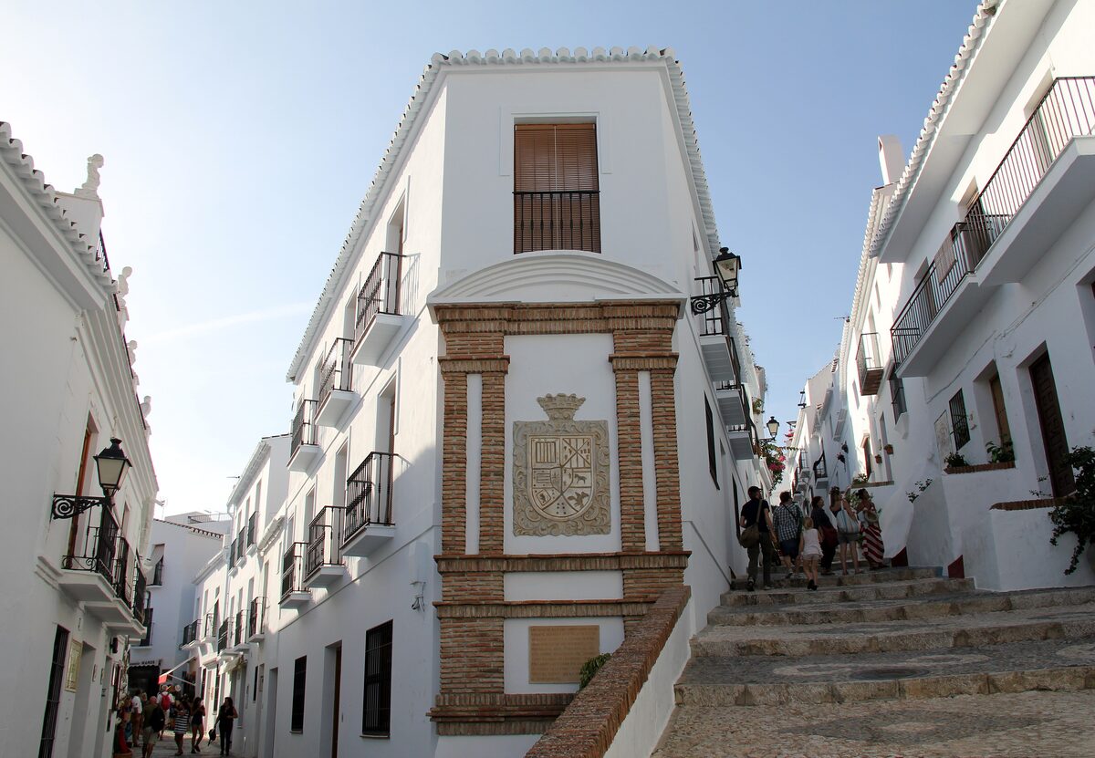 A steep whitewashed lane in Frigiliana with a stone staircase and a carved coat of arms on a wall