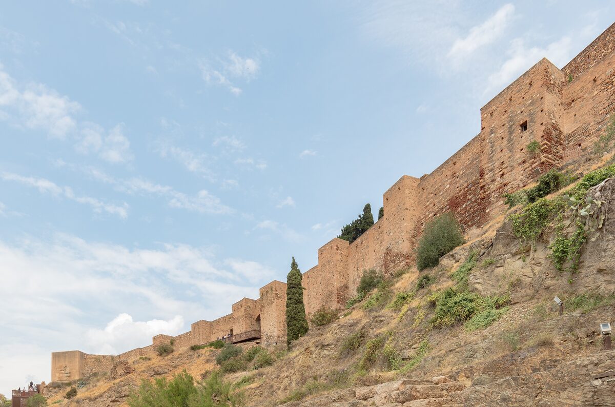 Long stone walls of Gibralfaro castle on the hillside, seen from below under a pale sky