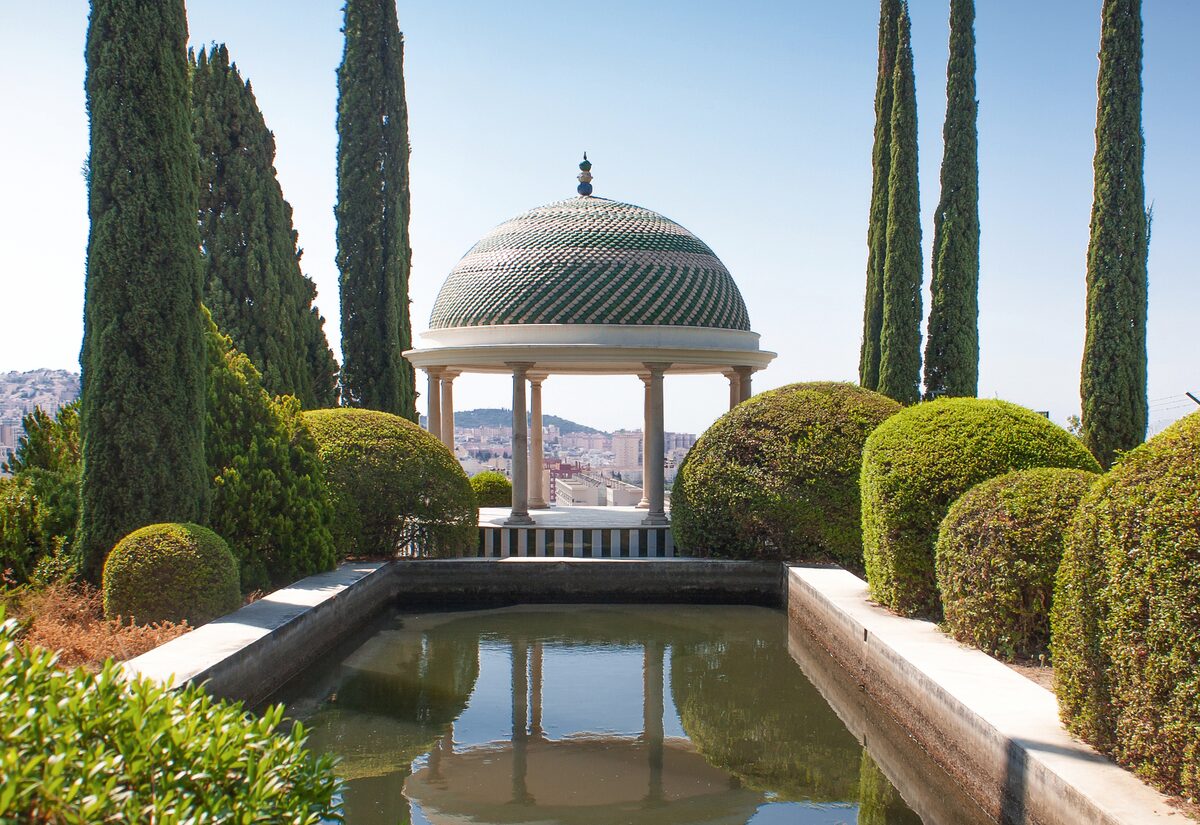 A domed garden pavilion beyond a long pool and clipped hedges between tall cypresses in La Concepción garden