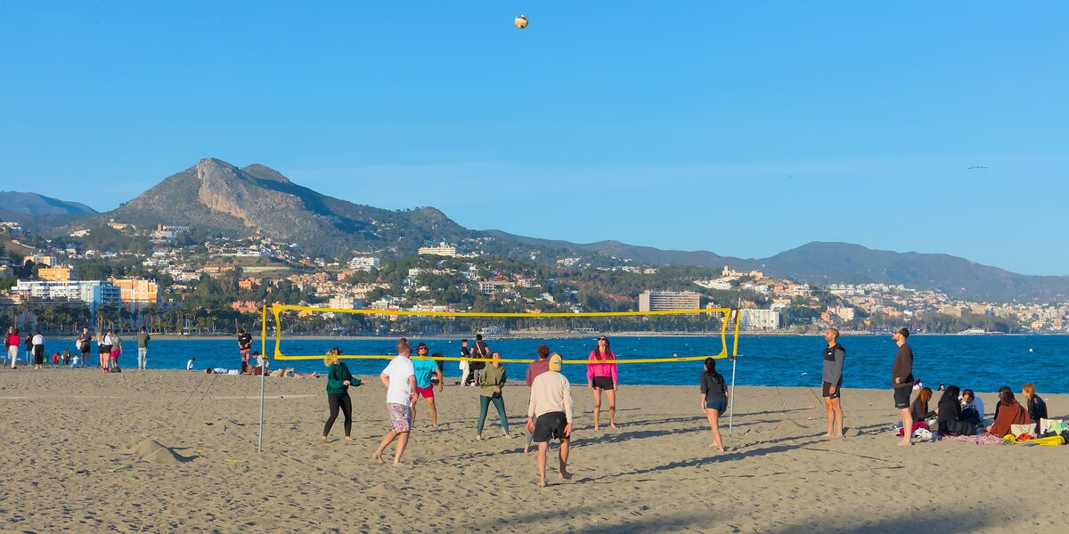 A volleyball game on La Malagueta beach, with the sea and mountains behind