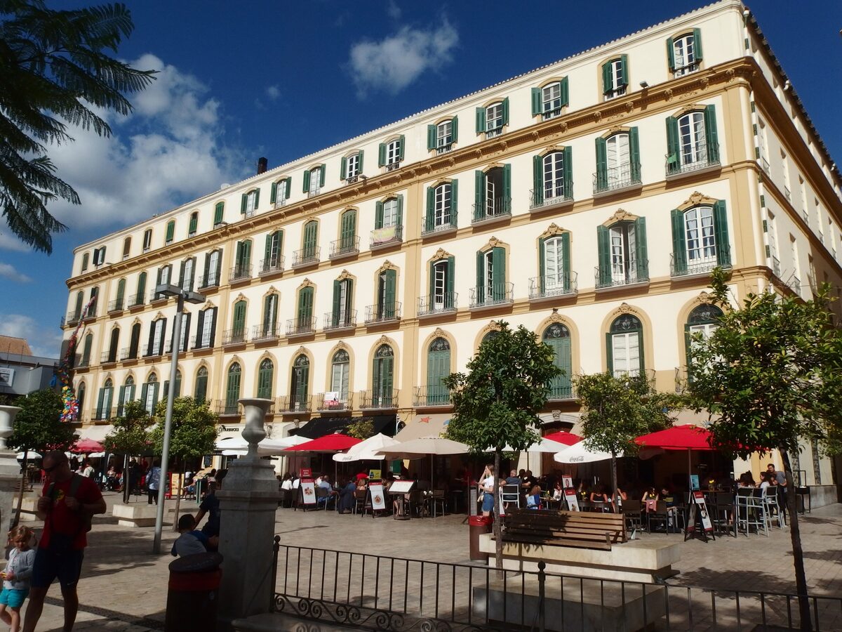 The yellow facade of Picasso's birthplace on the Plaza de la Merced, with green shutters and café tables in front