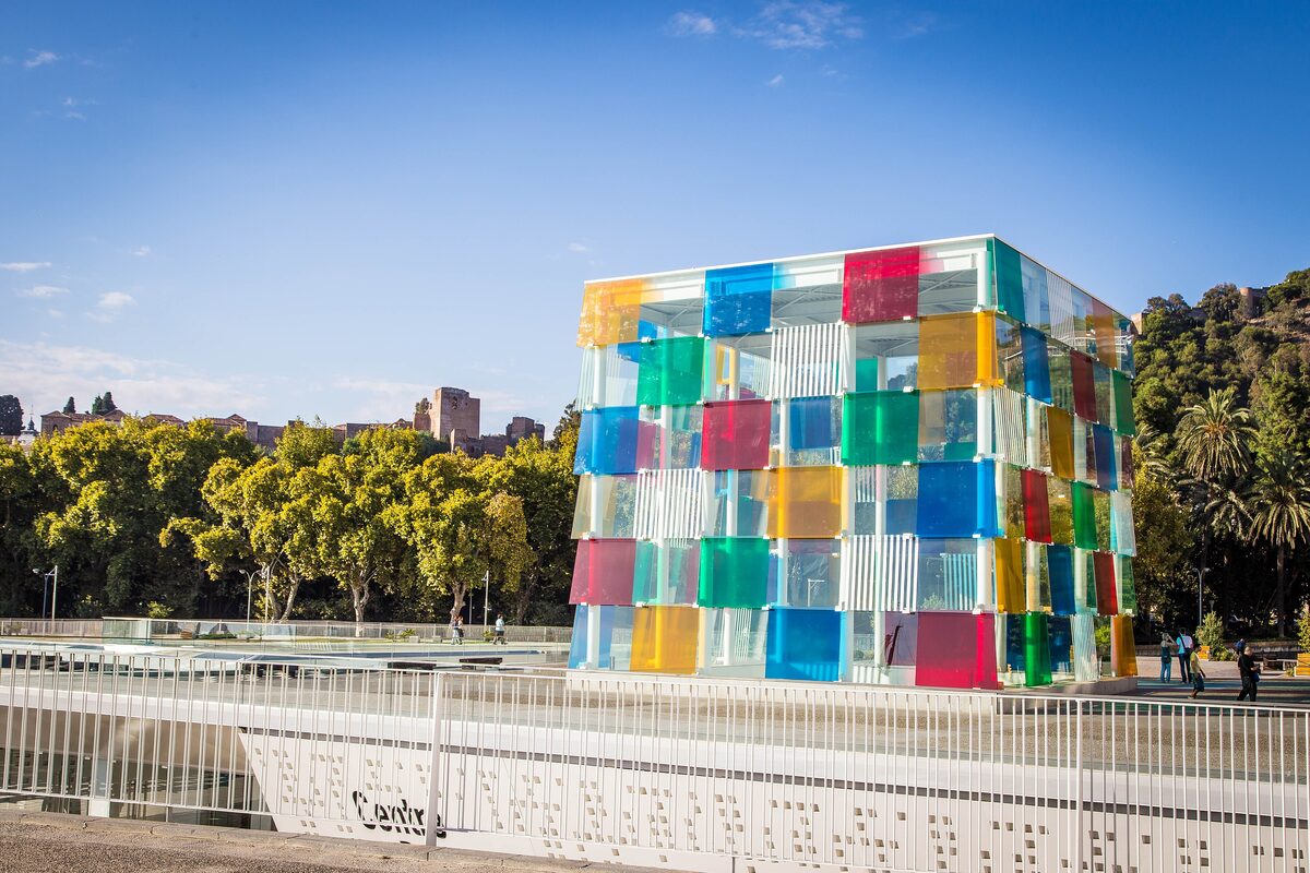 The colored glass cube of the Centre Pompidou Málaga on the port side, with trees and a railing in front
