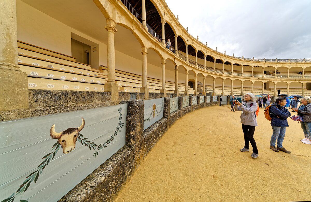 The sand ring and arcaded seats of the Ronda bullring, with a painted bull's head on the barrier