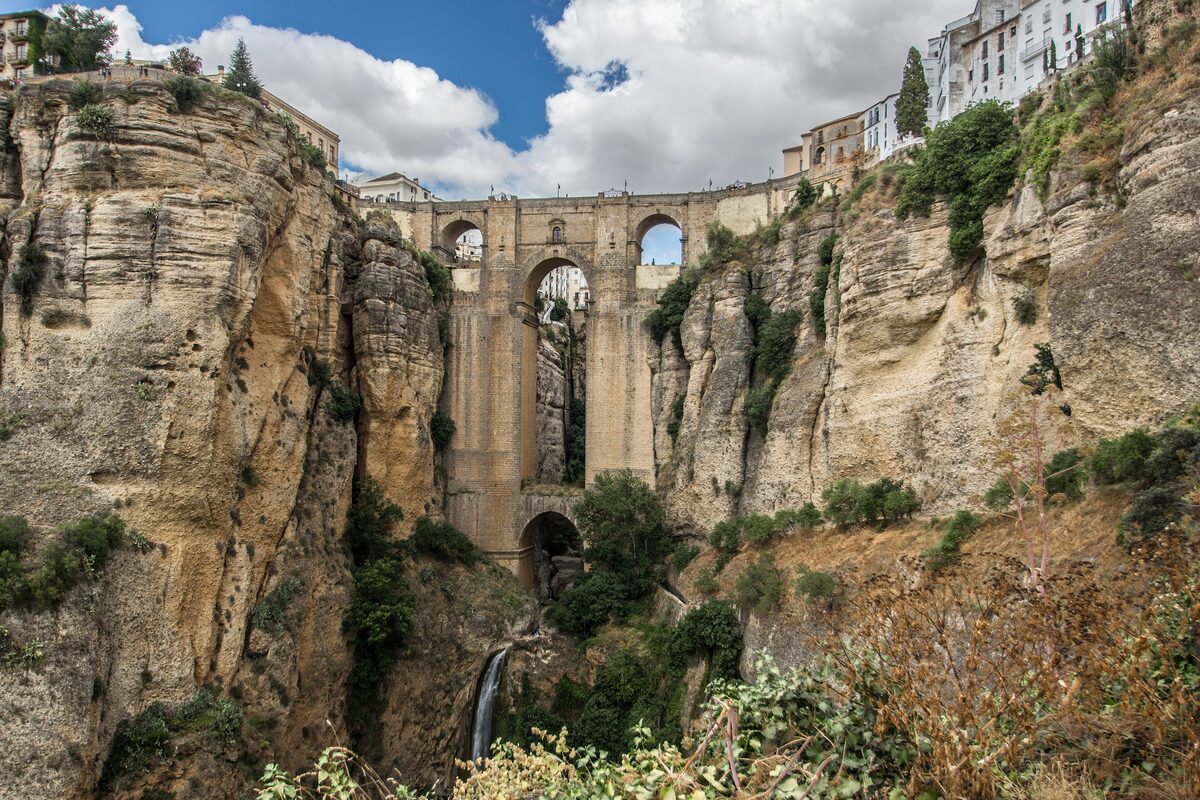 The Puente Nuevo arching between sandstone cliffs of the Ronda gorge, with a waterfall below and white houses on the rim