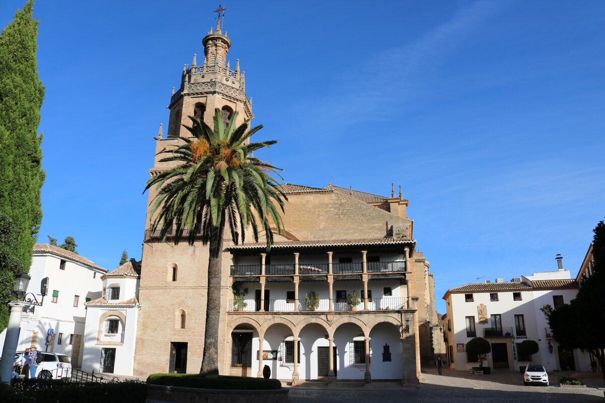 The arcaded facade and bell tower of Santa María la Mayor in Ronda, with a palm tree in front
