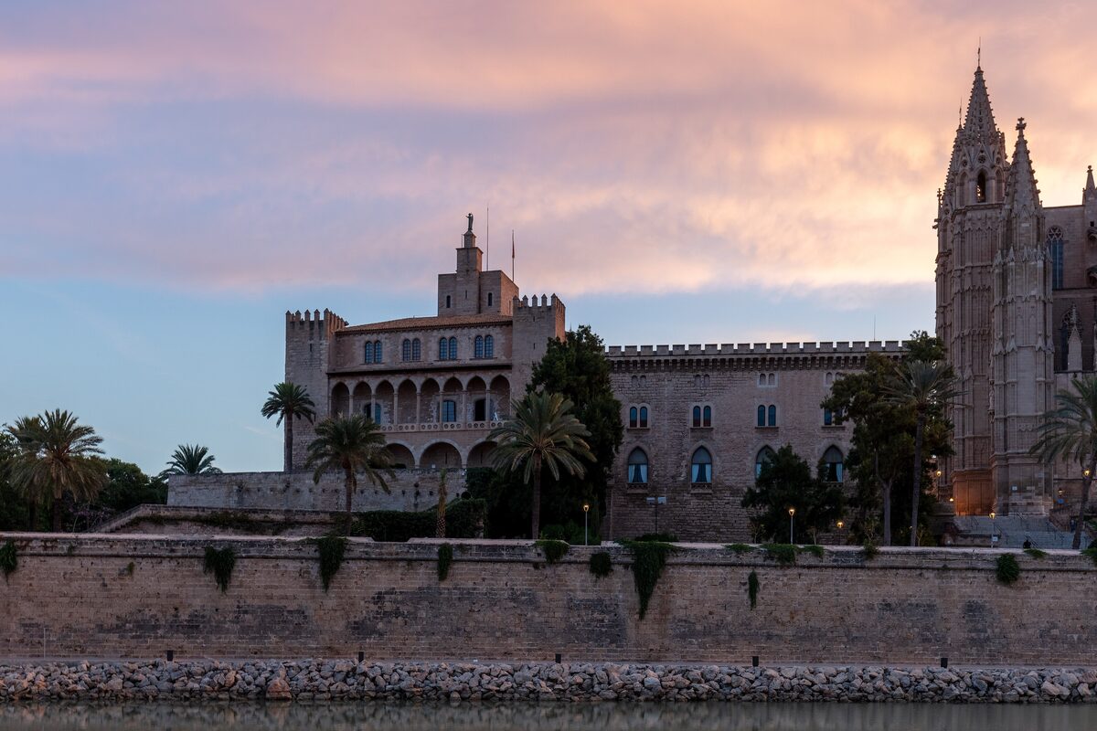 The Almudaina palace at sunset, a long sandstone block with towers beside the cathedral, lit pink by the evening sky