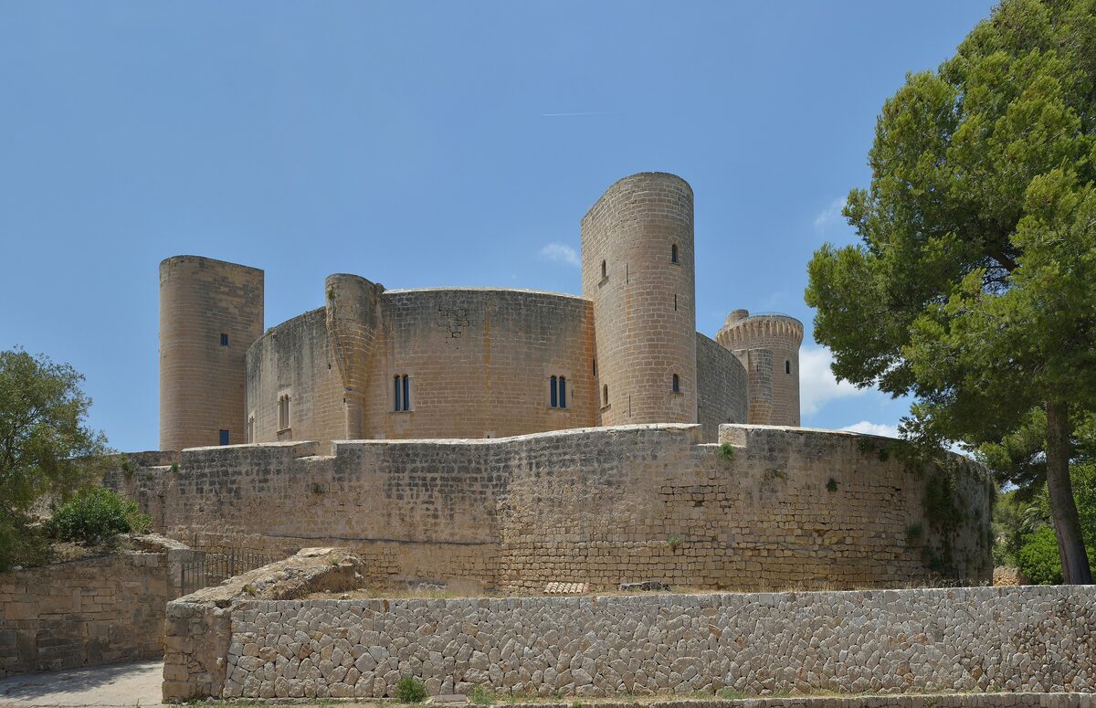 Bellver Castle, a round medieval fortress with a tall tower and thick walls on a pine-covered hill under a blue sky