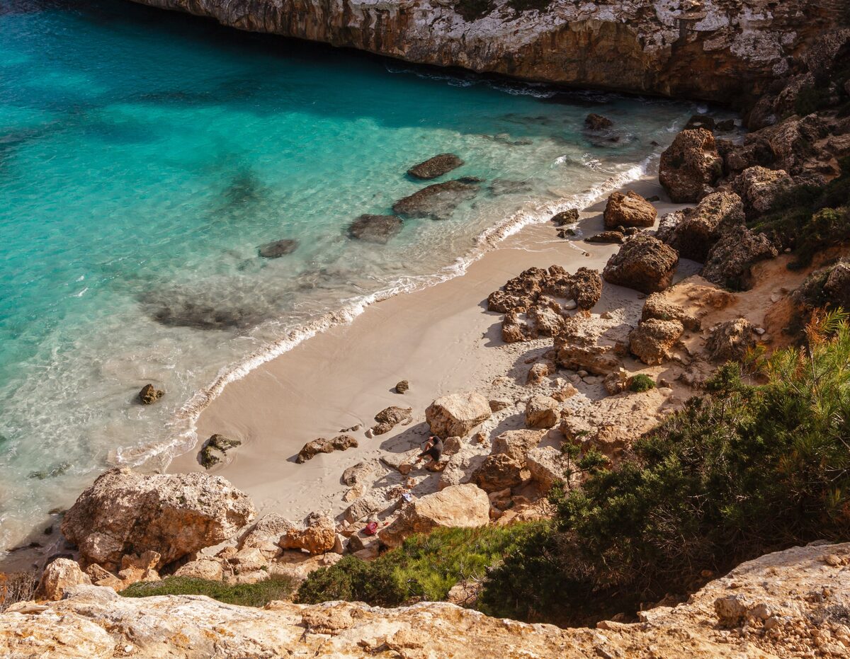 Caló des Moro, a small sandy cove with turquoise water between rocky cliffs and pine trees