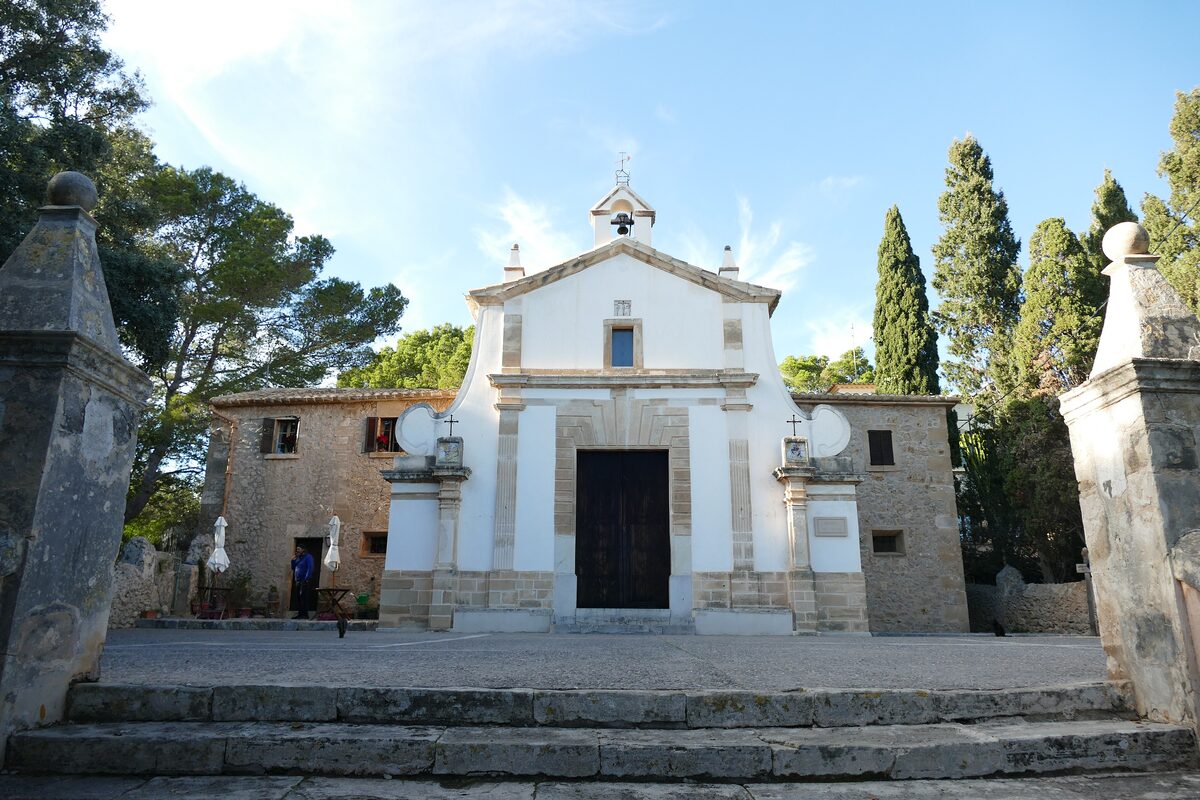 The white Calvari chapel at the top of its steps in Pollença, with a stone gateway and tall cypresses