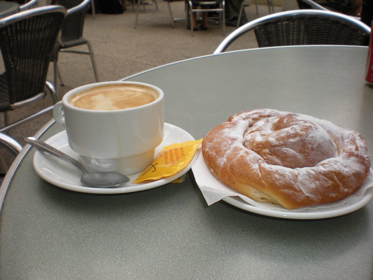 A coiled ensaïmada dusted with sugar on a plate beside a cup of café con leche