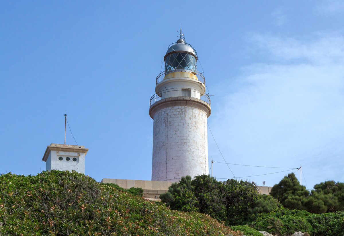 The white Far de Formentor lighthouse on the cape, with its keeper's building below and a blue sky