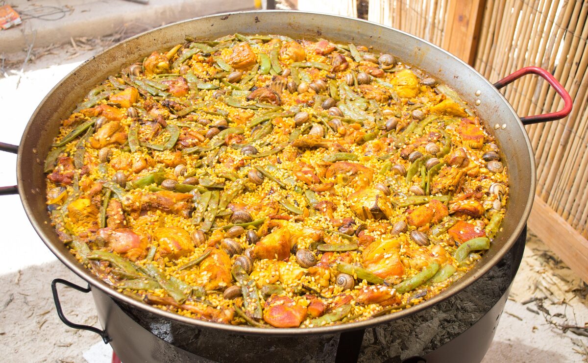 A large pan of paella valenciana with chicken, rabbit, green beans and white beans in saffron-yellow rice