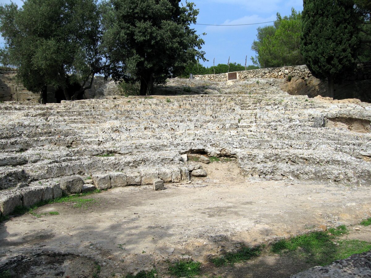 The Roman theatre of Pollentia: curved stone tiers and the flat orchestra, with olive trees behind