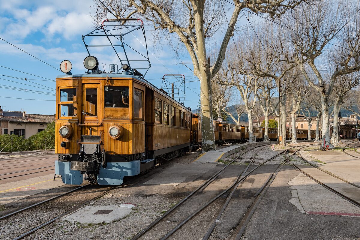 A vintage wooden Sóller railway carriage on the tracks at Sóller station, plane trees behind
