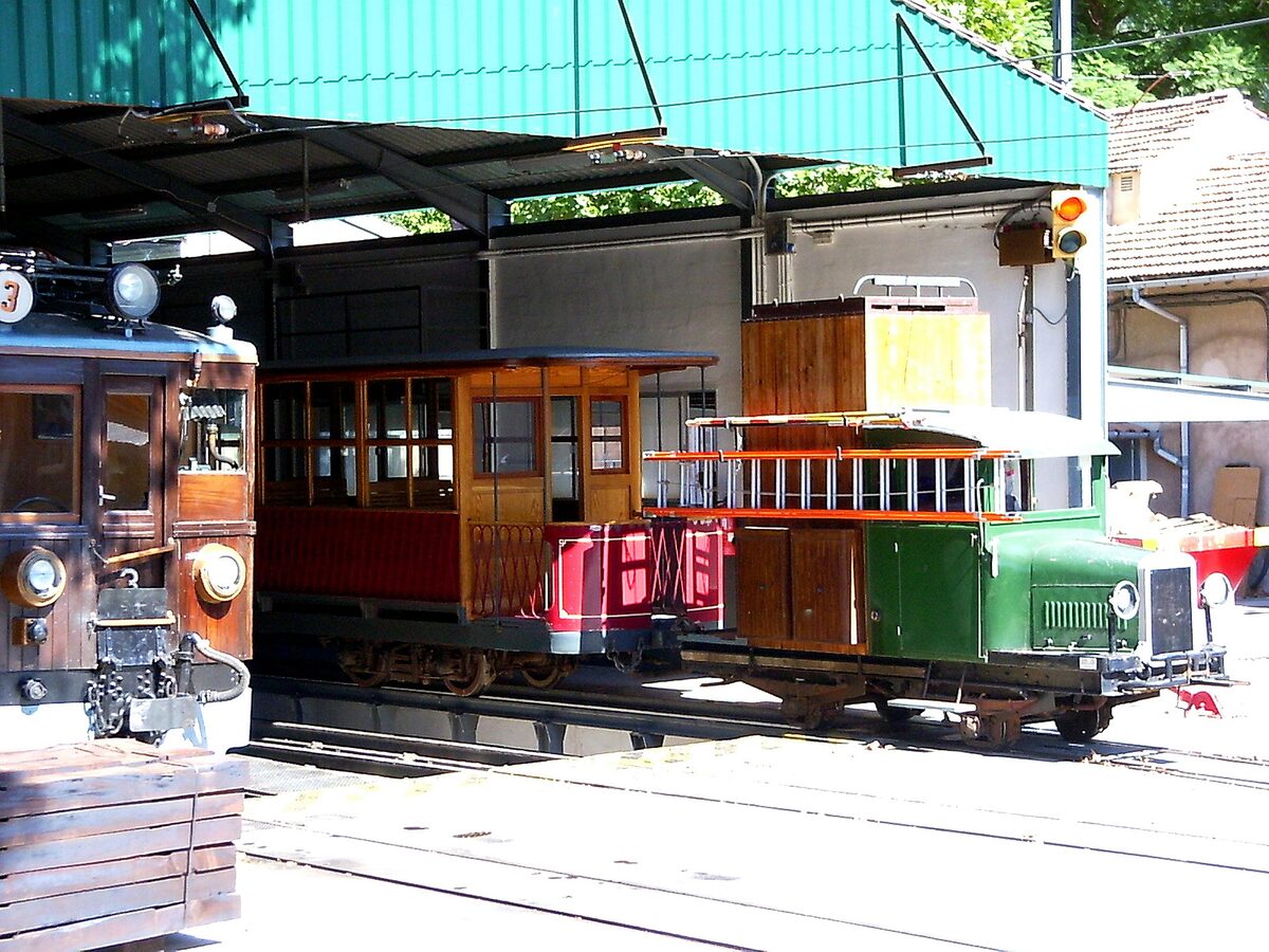 Old wooden tram cars with red and green bodies under a roof at the tram stop in Sóller