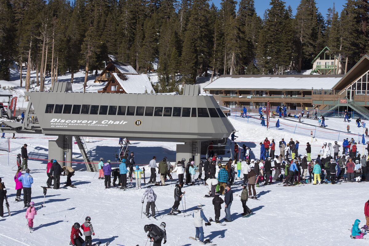 Skiers queue at the Discovery Chair terminal below a base lodge
