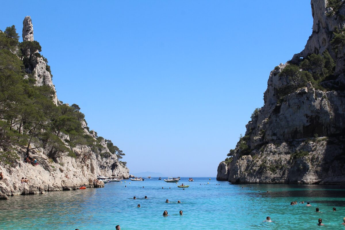 The turquoise water of the Calanque d'En-Vau between tall white limestone walls, with a few boats and, far off, swimmers