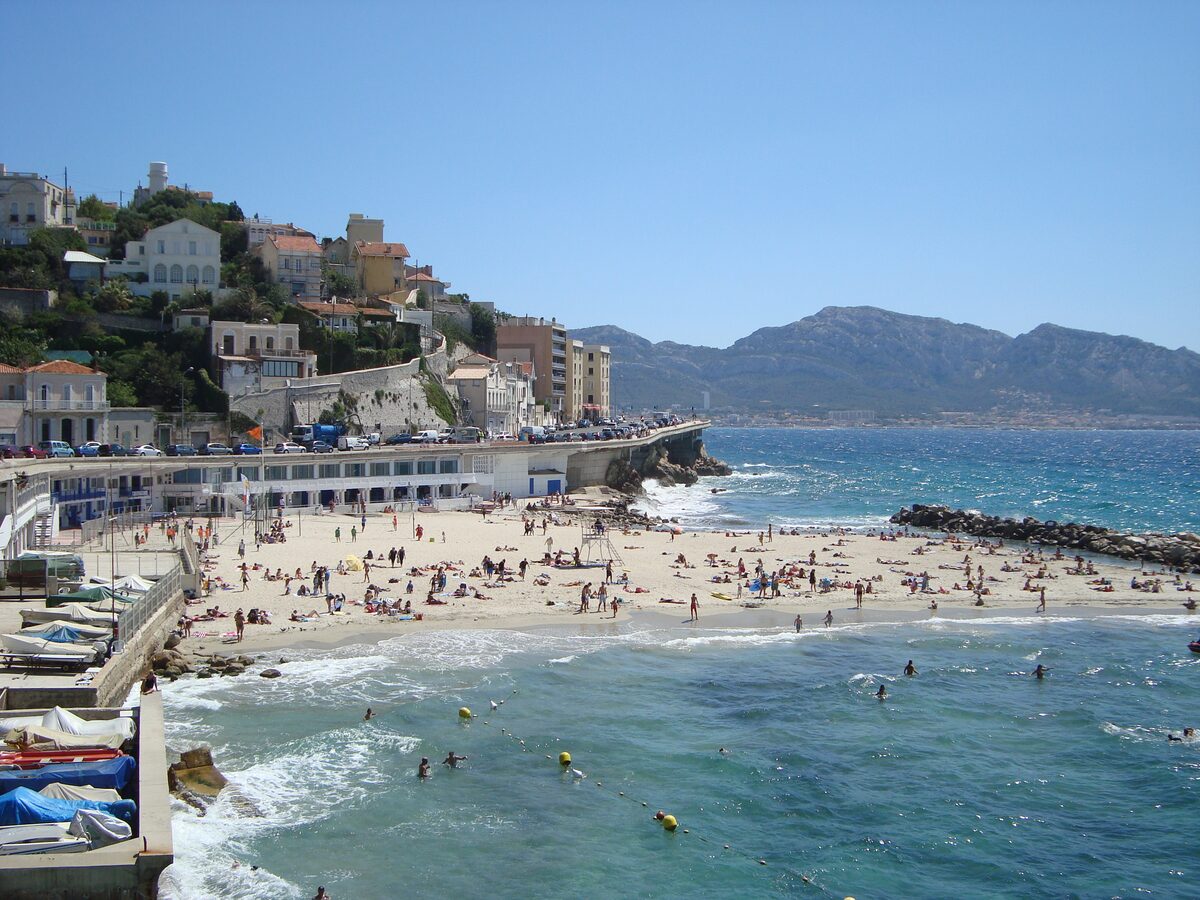 Swimmers on the sand of the Plage du Prophète, with the Corniche apartments above the bay