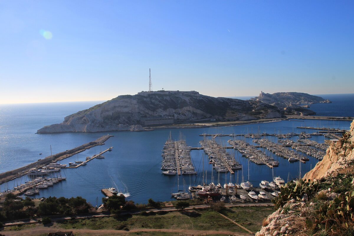 The marina of Port-Frioul packed with moored boats, with the white limestone hills of the Frioul islands behind
