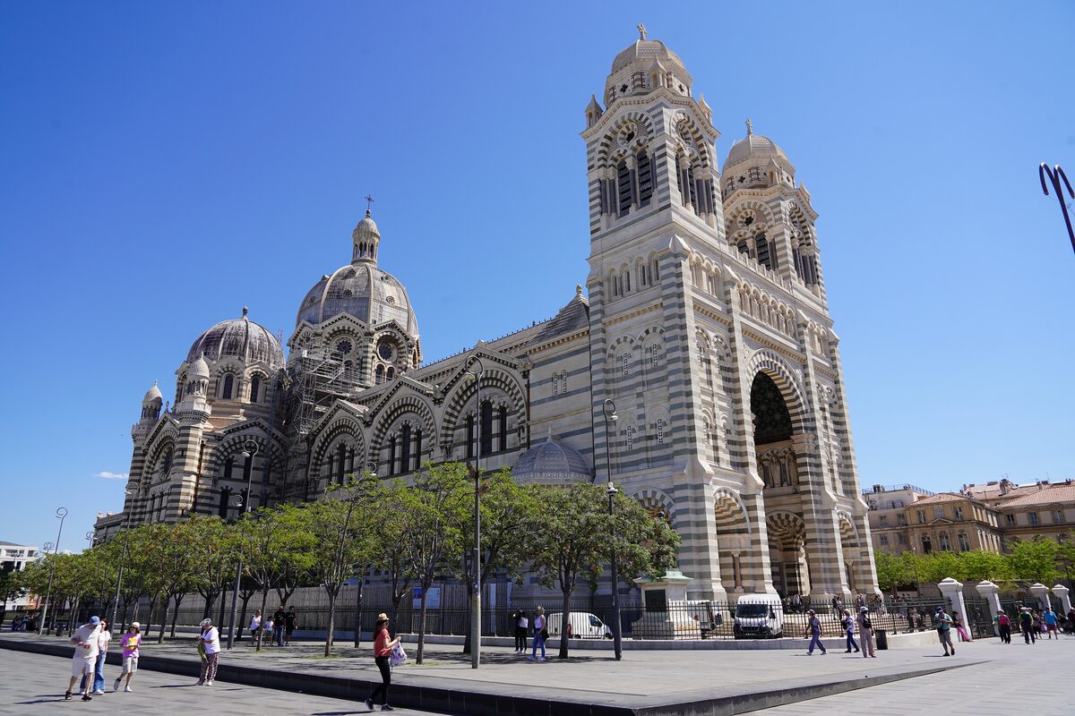 The striped stone domes and twin towers of the Cathédrale de la Major seen from its square on a clear day