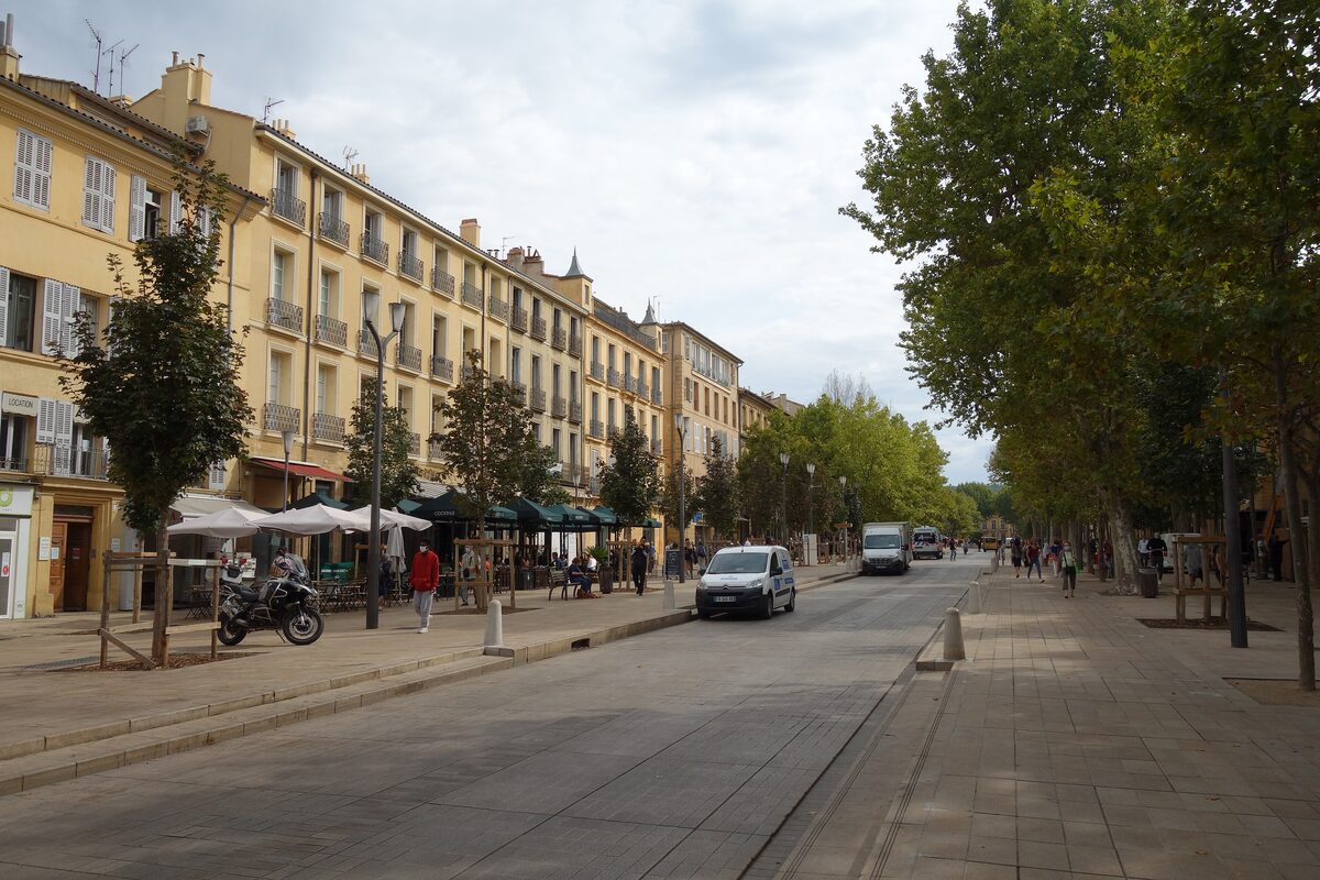 Plane trees on one side and honey-colored facades with café terraces on the other along the Cours Mirabeau in Aix-en-Provence