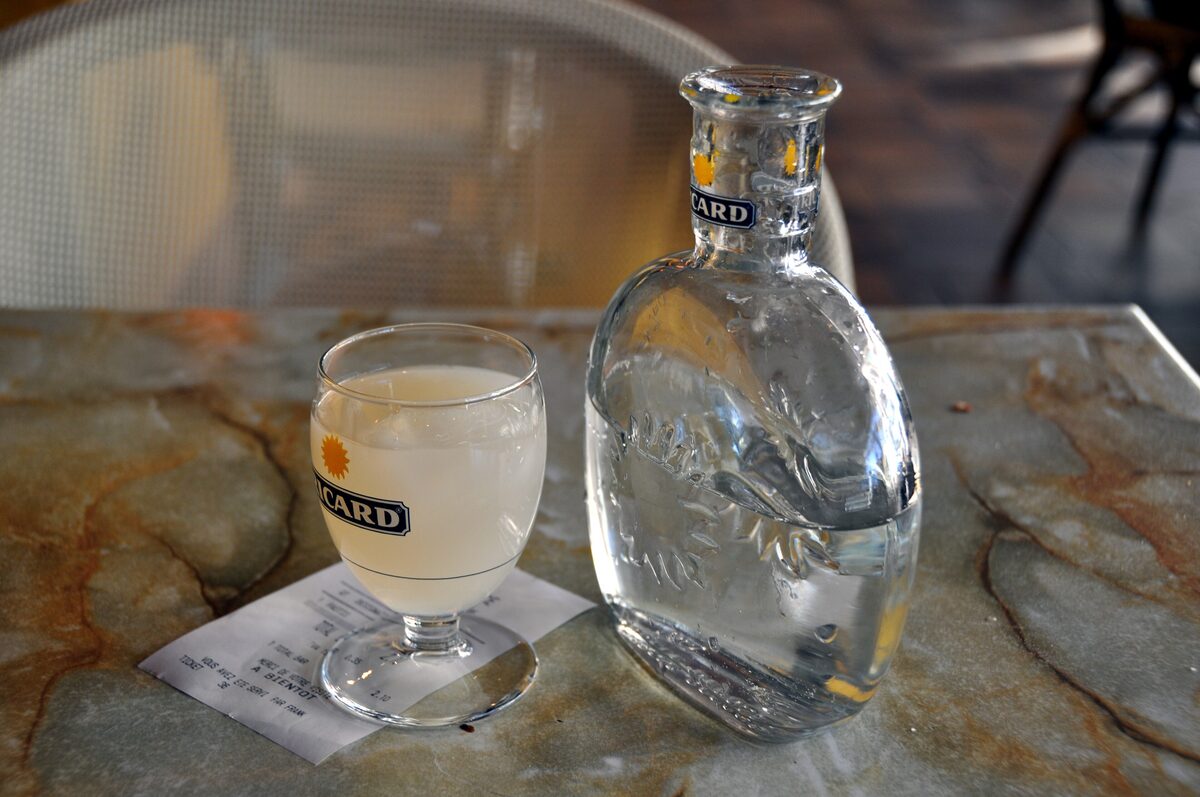 A glass of pastis beside a carafe on a stone café table