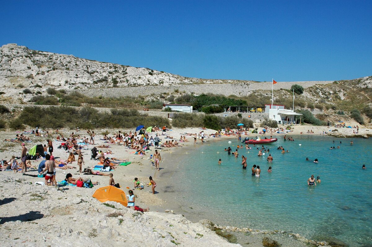 Swimmers in the clear shallow water of the Saint-Estève beach, with a white building on the shore