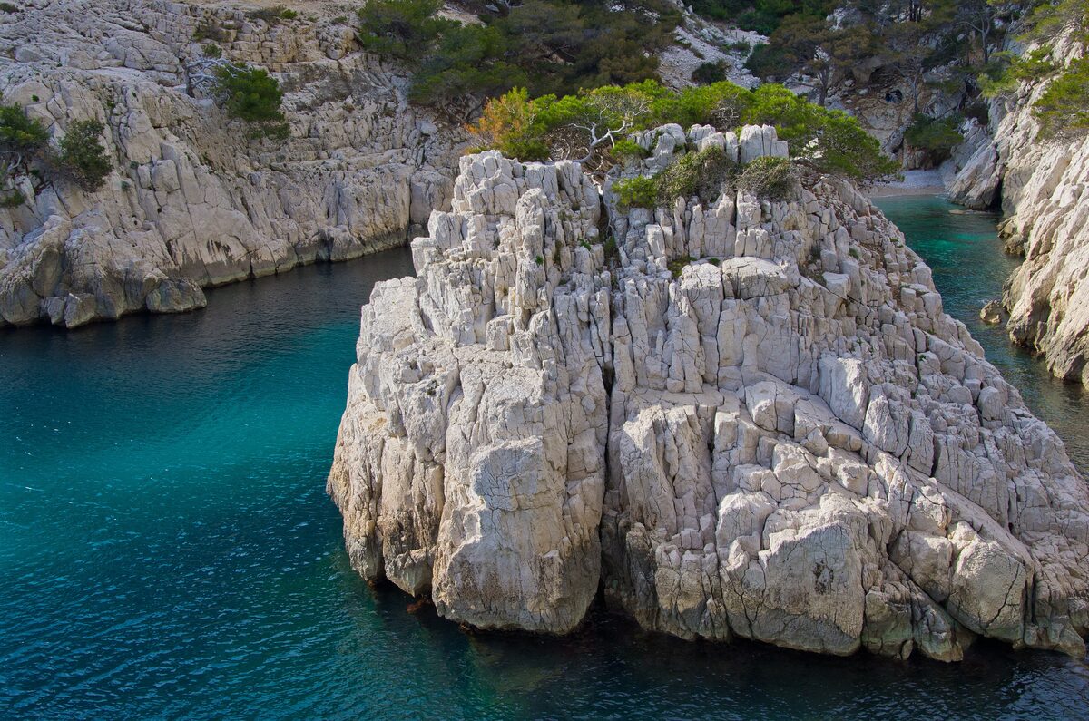 A clear green cove in the Calanque de Sugiton, with a tall white limestone rock standing in the water
