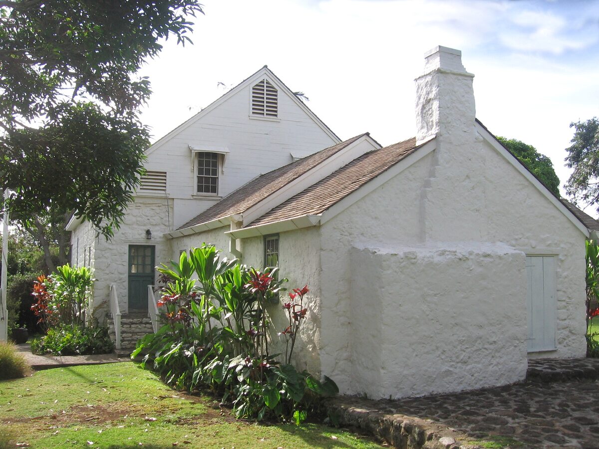 The whitewashed stone Bailey House in Wailuku with tropical flowers in the garden
