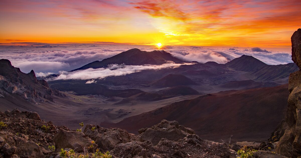 The sun rising over the clouds from the summit of Haleakalā, with the crater floor below