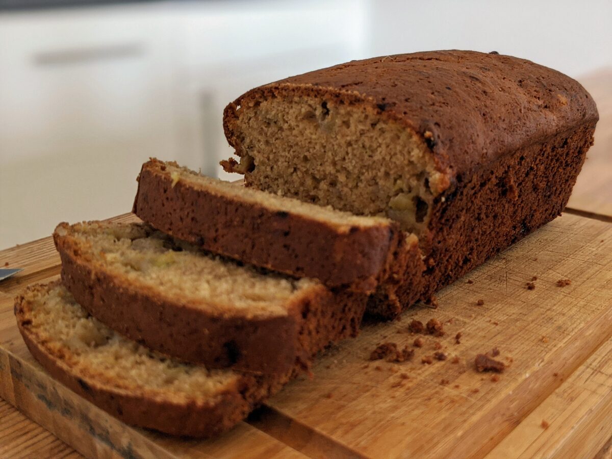 A loaf of banana bread with the first slices cut on a board