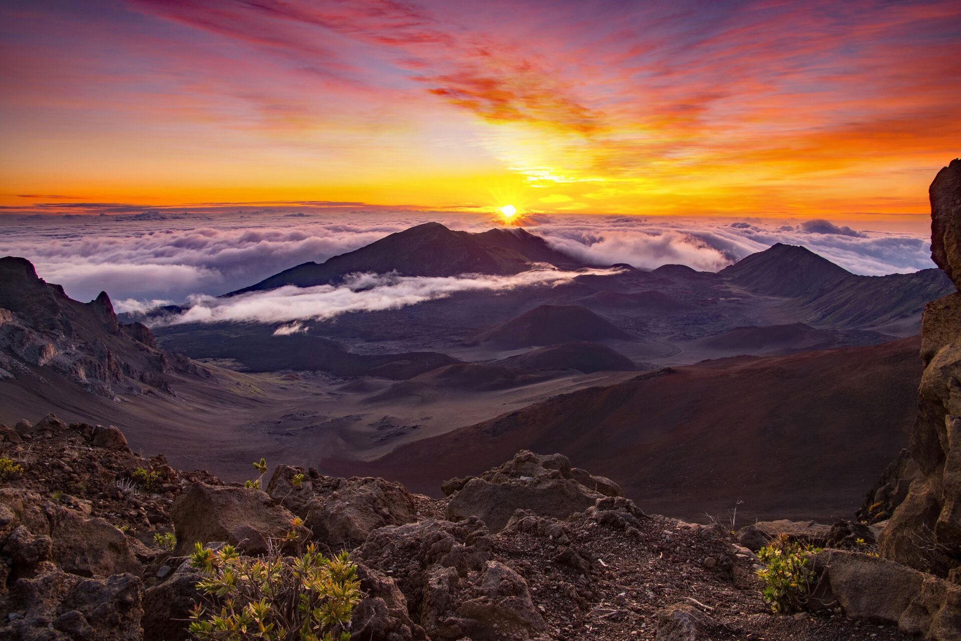The sun rising over the clouds from the summit of Haleakalā, with the crater floor below