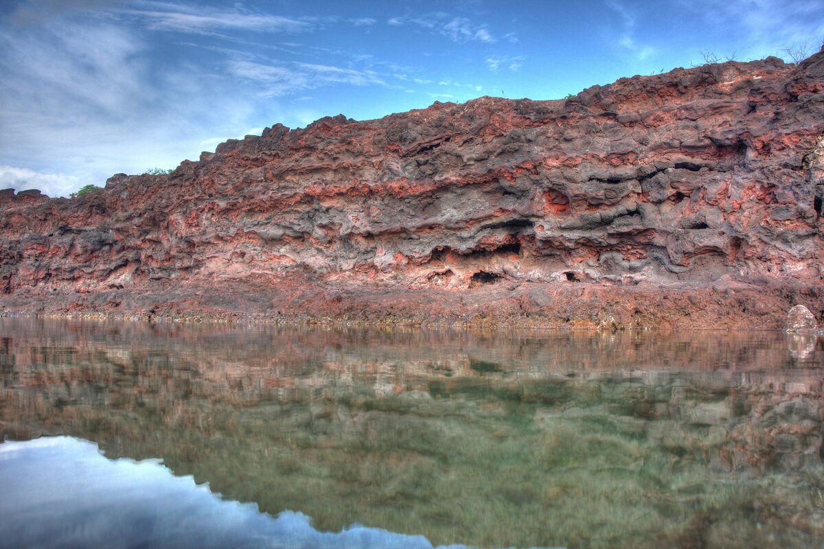 Red lava cliffs and a still tide pool at Hulopoʻe Bay on Lānaʻi