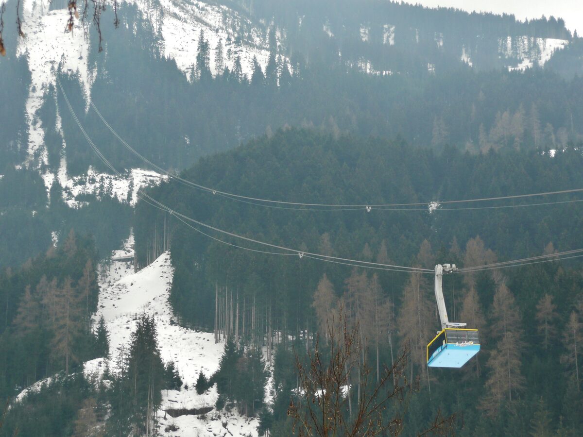 A gondola cabin on the Ahornbahn line over a snow-dusted forest on a hazy winter day