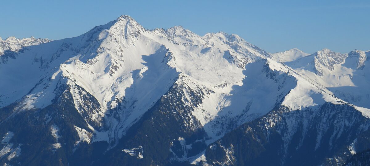 The snow-covered Ahornspitze massif in bright winter sunshine, with steep snowfields and dark forest below