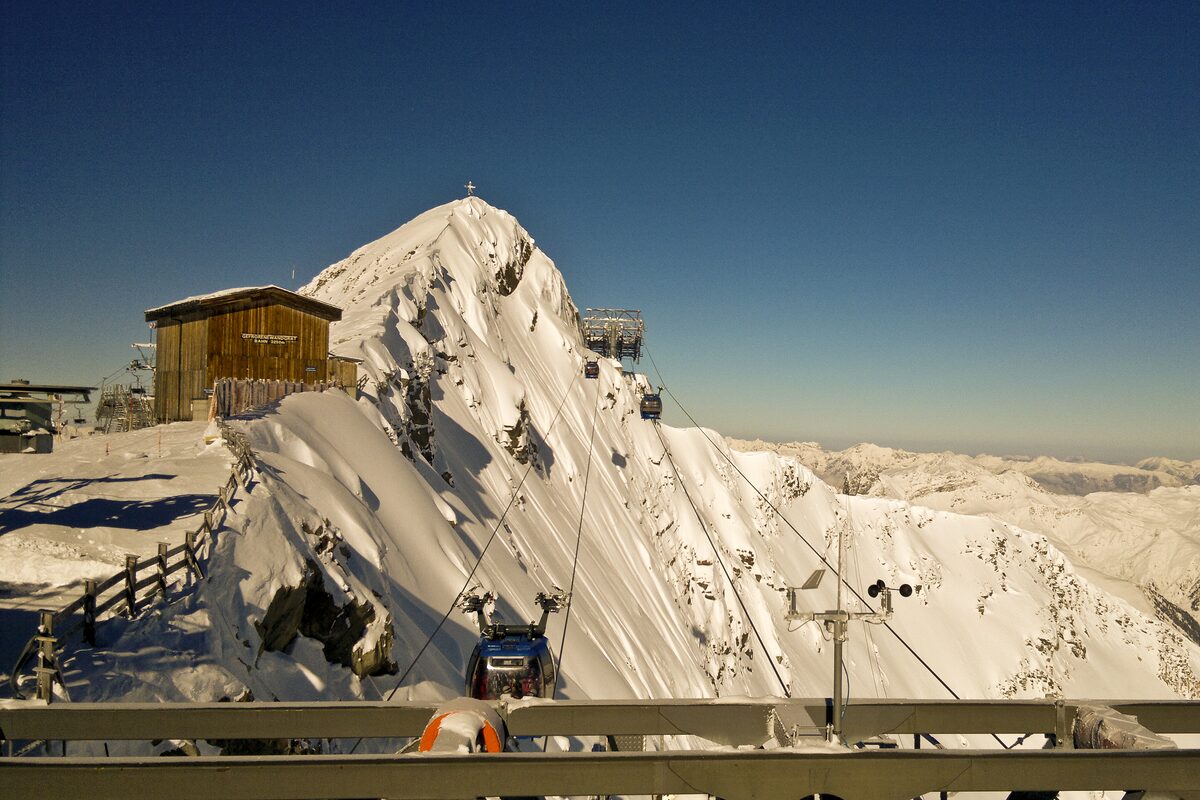 Gondola cabins climbing the snowy Gefrorene Wand to the wooden summit station at 3,250 m, in low winter sun under a deep blue sky