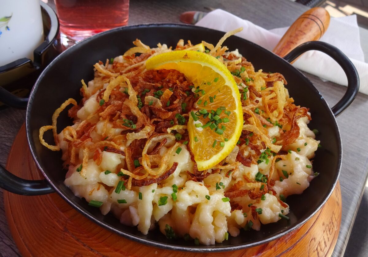 Käsespätzle in an iron pan, topped with crisp fried onions and a slice of lemon
