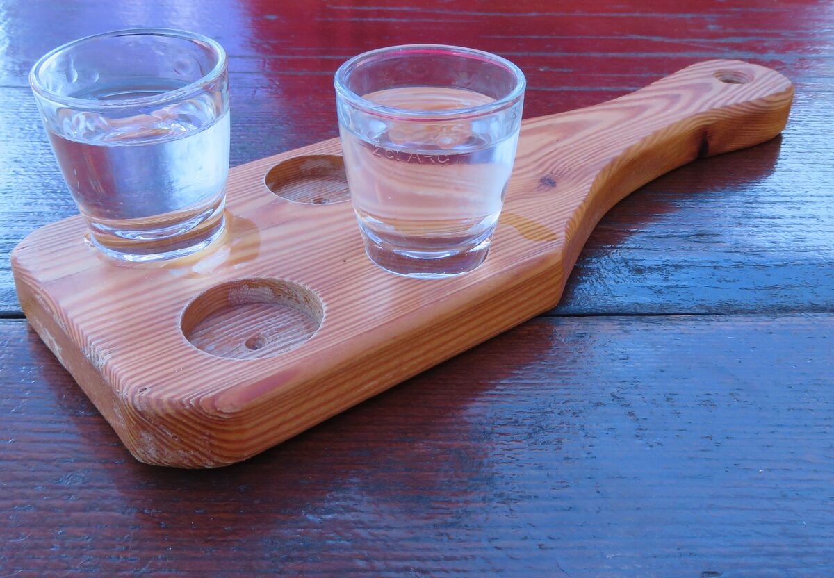 Two small glasses of clear fruit brandy on a wooden serving board