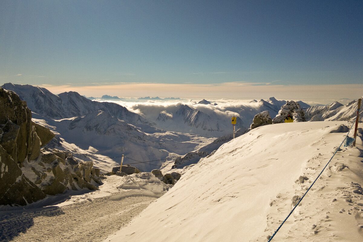 A snowy ridge and piste at 3,250 m above the Hintertux Glacier, with ranges of the Zillertal Alps and a sea of cloud in the distance