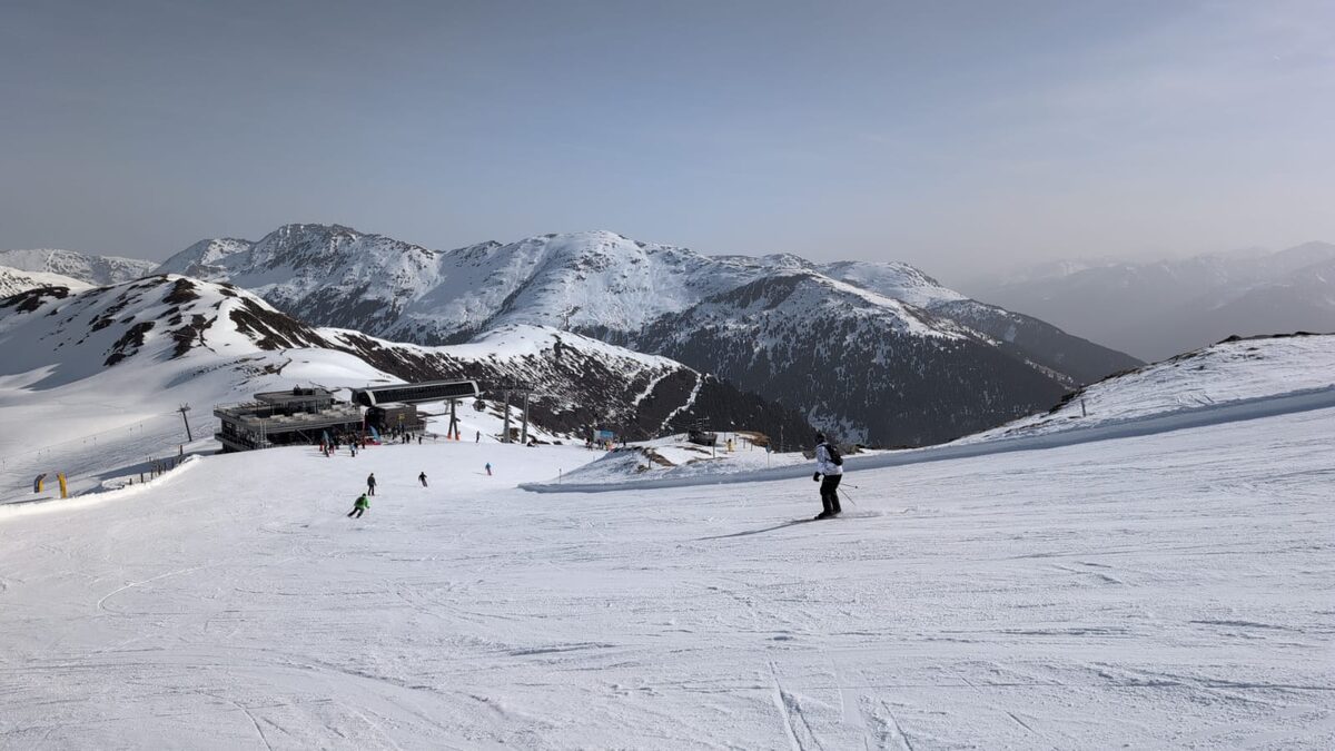 A skier on a wide snowy piste in the Zillertal Arena near Gerlos, with a lift station and snowy ridges behind