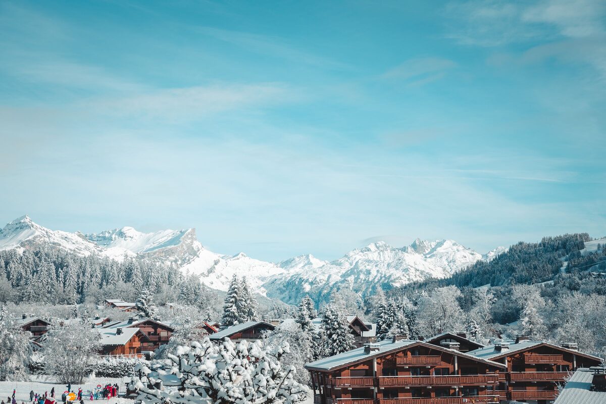 Snow-covered wooden chalets in Megève, with frosted trees and the white peaks of the Alps behind