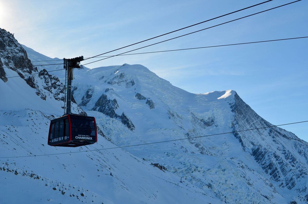 A red cable car cabin of the Aiguille du Midi lift climbing over snowy rock above Chamonix